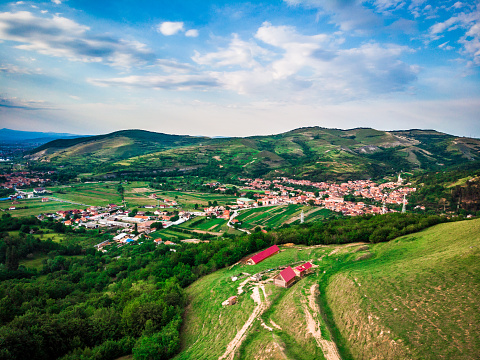High angle drone shot depicting the architecture - the small cottages and houses - of a traditional village in Transylvania, Romania. A road cuts directly through the image and we can see people's gardens, which they mainly use for growing vegetables. The village is surrounded by a lush green, beautiful rural landscape. Room for copy space.