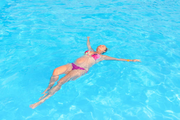 Happy middle-aged woman in black bikini standing in the sea with arms raised, enjoying a refreshing and joyful moment at the beach