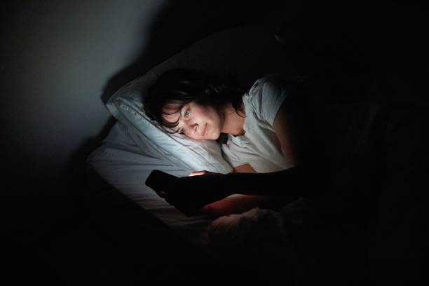 istock Young woman checking her cellphone while lying in bed at night 1249145235