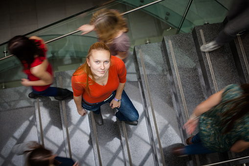 At the university/college - Students rushing up and down a busy stairway - confident pretty young female student looking upwards