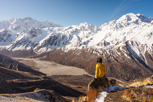 A trekker sitting on top of Kyanjo Ri view point and enjoying landscape of Langtang valley. Himalaya mountains range in Nepal, Asia