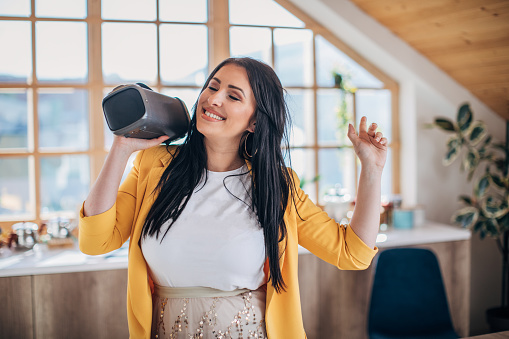 Woman dancing at home while holding wireless speaker