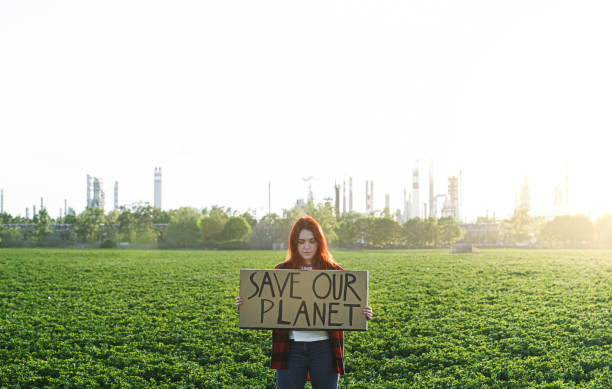 istock Young woman activist with placard standing outdoors by oil refinery, protesting. 1249150148