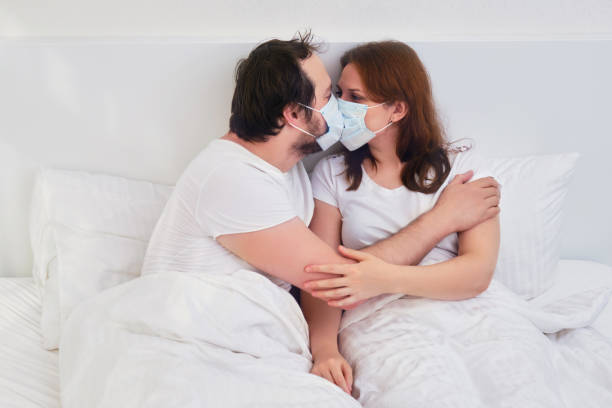 coppia che si bacia a letto con la maschera medica. relazioni familiari isolate a causa del coronavirus. - cold and flu flu virus bed couple foto e immagini stock