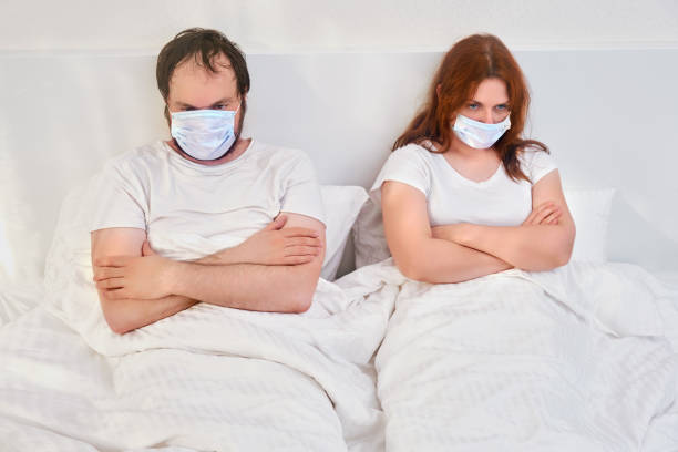 o casal brigou e deita na cama com máscaras médicas. problemas familiares devido ao isolamento da quarentena devido à pandemia coronavírus. - cold and flu flu virus bed couple - fotografias e filmes do acervo