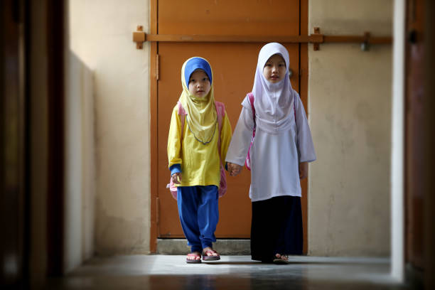 Muslim sisters in their school uniform are holding hands gearing ready to back to school in Malaysia.