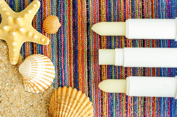 Three lip balms, sunscreen sticks on the colorful beach towel with sand and seashells. Summer lip treatment and UV protection concept. Close up, flat lay, copy space Three lip balms, sunscreen sticks on the colorful beach towel with sand and seashells. Summer lip treatment and UV protection concept. Close up, flat lay, copy space vitamin b 3 stock pictures, royalty-free photos & images