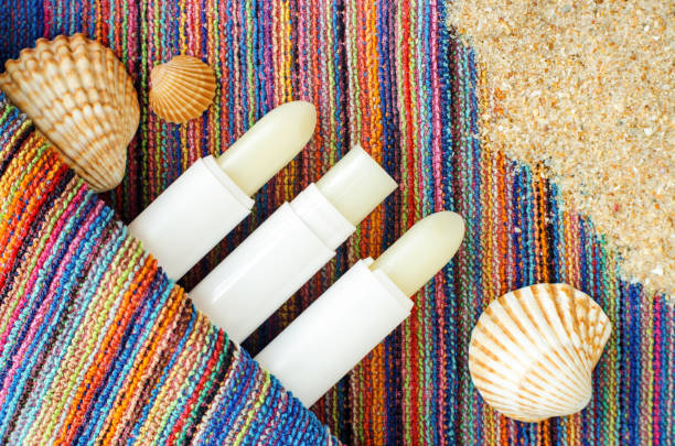 Three lip balms, sunscreen sticks on the colorful beach towel with sand and seashells. Summer lip treatment and protection concept. Close up, flat lay, copy space Three lip balms, sunscreen sticks on the colorful beach towel with sand and seashells. Summer lip treatment and protection concept. Close up, flat lay, copy space vitamin b 3 stock pictures, royalty-free photos & images