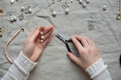 Jewelry designer working in studio with tools making pearl earrings. Close-up of female hands working with jewelry tools