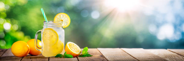 Cold Glass Of Lemonade Cold Glass Of Lemonade On Wooden Table With Lemons, Tea Leaves And Sunlight straw photos stock pictures, royalty-free photos & images
