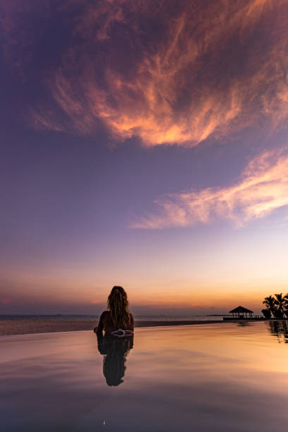 istock Back view of a woman relaxing in infinity pool at sunset. 1249163666