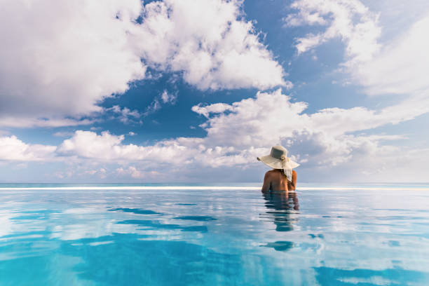 istock Rear view of a woman with sun hat looking at view from an infinity pool. 1249164896