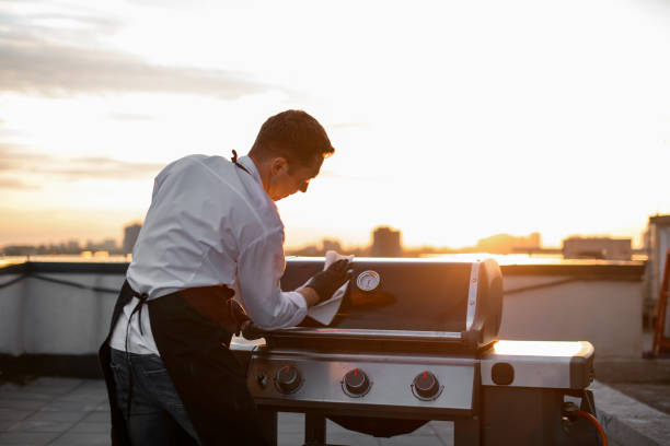 cook man wipes the grill equipment for barbecue cook man in black gloves and aprons wipes the grill equipment for barbecue. Sunny sunset metal grate stock pictures, royalty-free photos & images