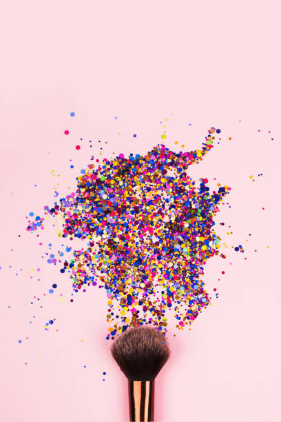 Vertical composition with professional cosmetic makeup brush with explosion of shiny colorful sparkles on bright pink background with copyspace for your text. Creative make-up concept