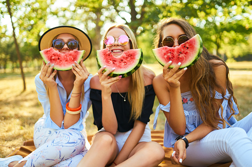 Three nice girls having fun eating watermelon In the park. Excellent sunny weather. Beautiful figures. Super mood. Summer concept.
