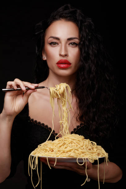 istock A beautiful girl eats with a fork spaghetti with red lips. 1249181750