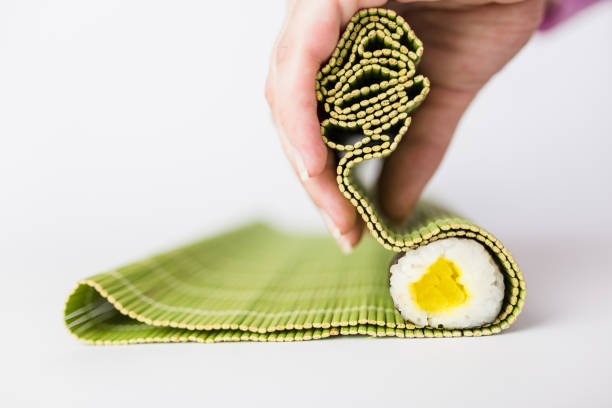 Close up of chef hands rolling up sushi on a bamboo mat isolated on white background. Japanese meal preparation.
