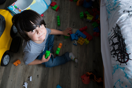 Latino boy from Bogota Colombia between 2 and 4 years old looks at the camera in a portrait while playing on the floor of his room with toys during the quarantine generated by the Covid 19