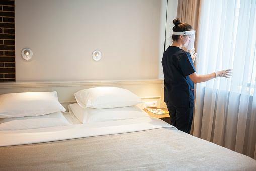 Maid preparing room for guest's, wearing a facemask while working at a hotel