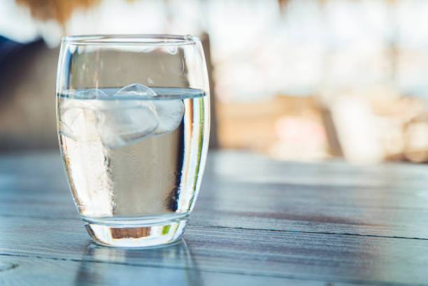 Glass of water with ice cubes Close up of glass of water with ice on a wooden table. cafe transparent glass table stock pictures, royalty-free photos & images