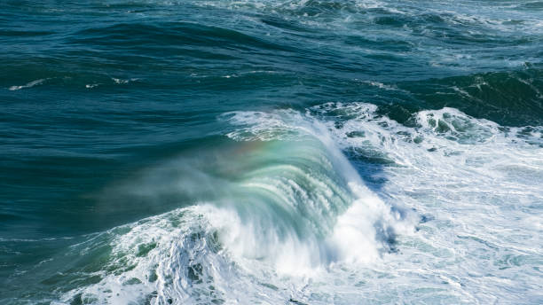 istock Giant ocean waves crash on the water surface forming a rainbow 1249199012