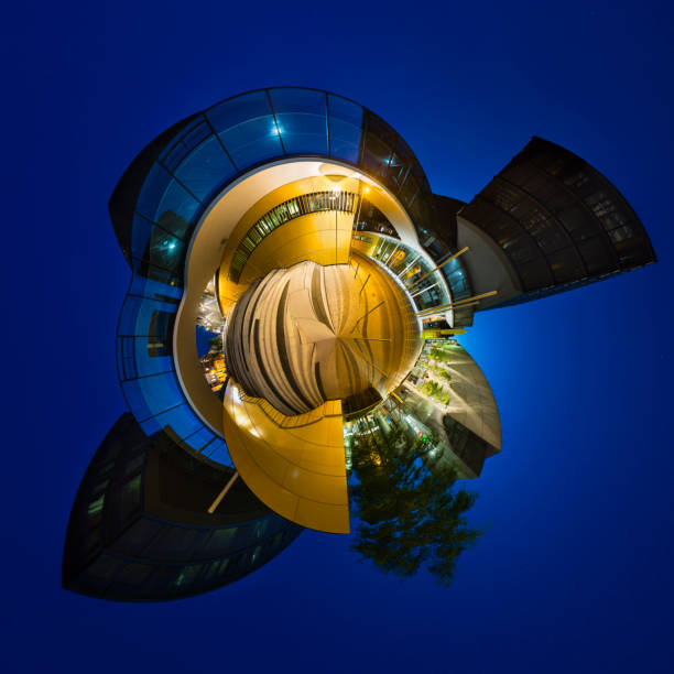 Little planet panorama of modern glass architecture with bridges crossing a street and a staircase in the center of Aachen, Germany with night blue sky.