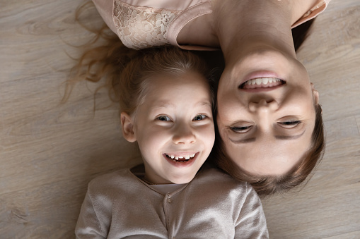 Close up top view portrait of smiling young Caucasian mother and small daughter lying on floor relaxing, happy mom or nanny have fun play rest with little girl child, family unity, bonding concept