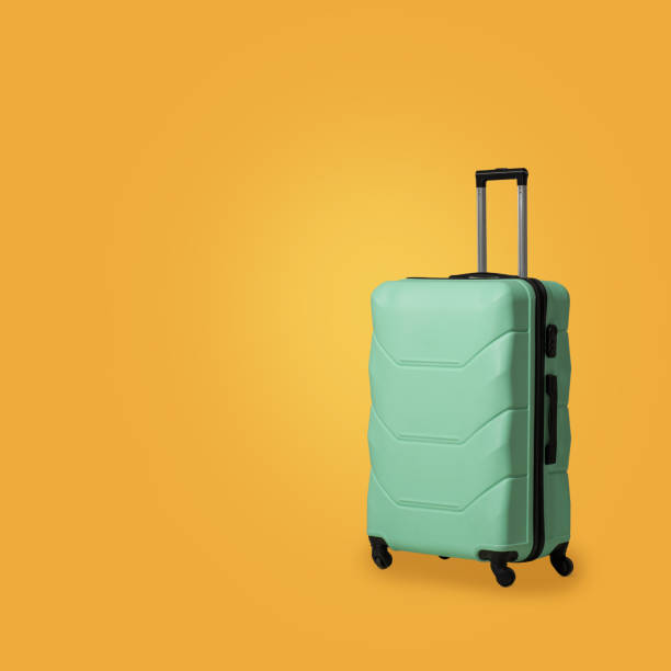 Green plastic suitcase with wheels isolated on sunny yellow background. Mint green polycarbonate case for safe storage of luggage. Blank or template for advertising travel agencies