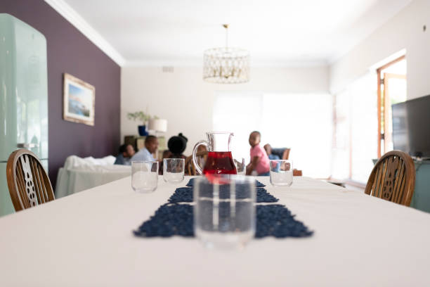 Foreground glasses and juice jug on dinner table family in background chatting in the living room