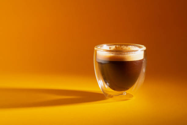 istock Freshly brewed creamy espresso in a glass coffee cup isolated on yellow background, close up with copy space 1249202425
