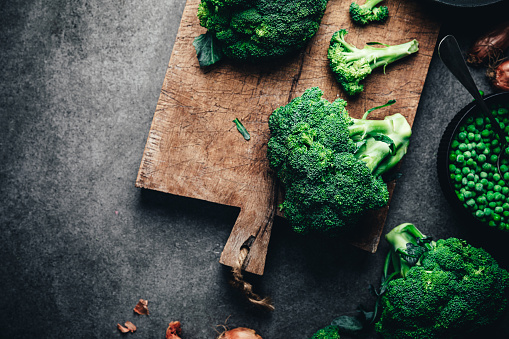 Directly above shot of fresh broccoli on chopping board with green peas bowl. Ingredients for making green vegan soup in kitchen.