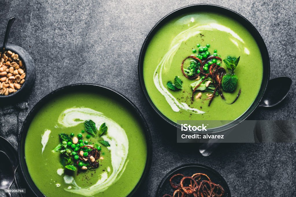 Green peas cream soup Green peas cream soup in dark plate. Directly above shot of vegetarian green cream soup of green peas with seeds and mint leaves on kitchen counter. Soup Stock Photo