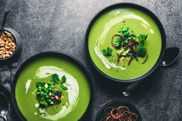 Green peas cream soup Green peas cream soup in dark plate. Directly above shot of vegetarian green cream soup of green peas with seeds and mint leaves on kitchen counter. cooking pan photos stock pictures, royalty-free photos & images