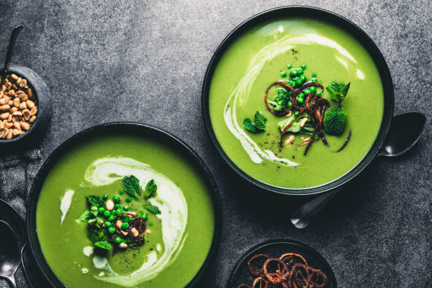 Green peas cream soup Green peas cream soup in dark plate. Directly above shot of vegetarian green cream soup of green peas with seeds and mint leaves on kitchen counter. green pea stock pictures, royalty-free photos & images