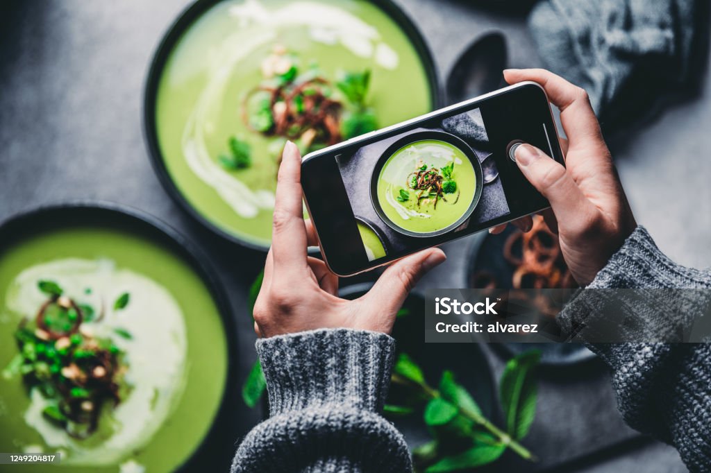 Woman photographing fresh green soup Close-up of a woman taking a photo of green cream soup with her mobile phone. Female hand photographing green soup. Food Stock Photo