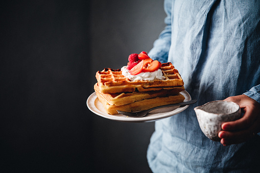 Close-up of a woman's hands holding a plate with waffles and fresh berries. Female with tasty breakfast.