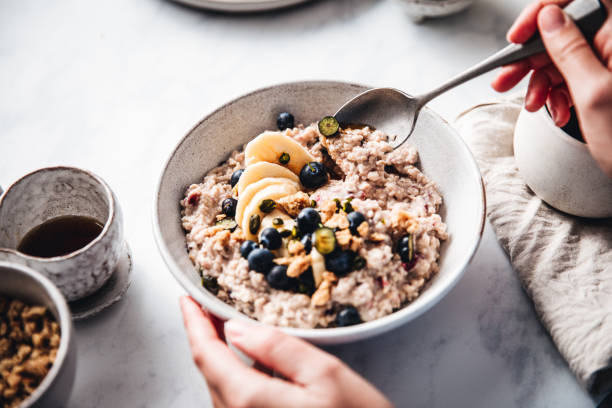 Woman making healthy breakfast in kitchen Close-up of a woman mixing oats flour, banana and blueberries in a bowl. Female making healthy breakfast in kitchen. bowl stock pictures, royalty-free photos & images