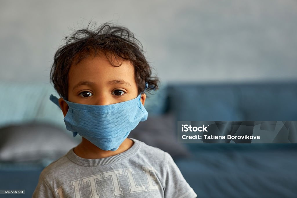 Portrait of a cute african american boy in mask at home - contagion of the Novel Coronavirus 2019- ncov - virus incubation isolation Protective Face Mask Stock Photo