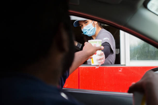 Drive Thru Prince Rupert, Canada - May 17, 2020. A man reaches for his food at the McDonalds drive-thru window as the employee wears a mask for protection. fast food restaurant stock pictures, royalty-free photos & images