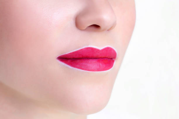 istock Young woman having permanent makeup on her lips at the beauticians salon. Permanent Makeup (Tattoo). drawing a contour with a white lip pencil 1249216275