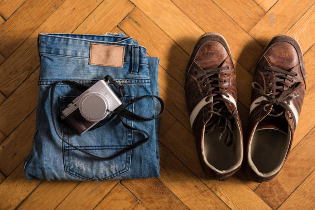 A pair of fretted blue jeans, brown shoes, and a camera lie by on the floor.
