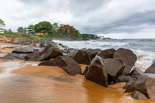 Beach with red sand and red rocks with a dramatic sky in Congo Town, Monrovia, Liberia