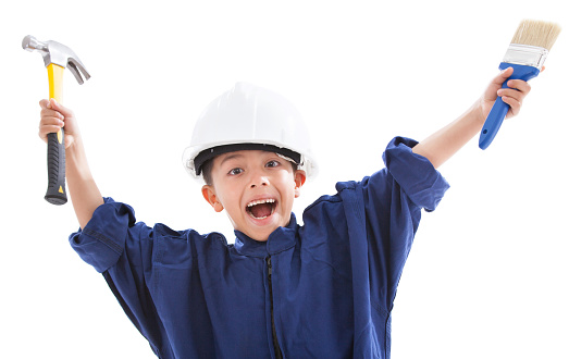 Excited cute little boy dressed up as a contractor smiling at camera holding tools with arms up