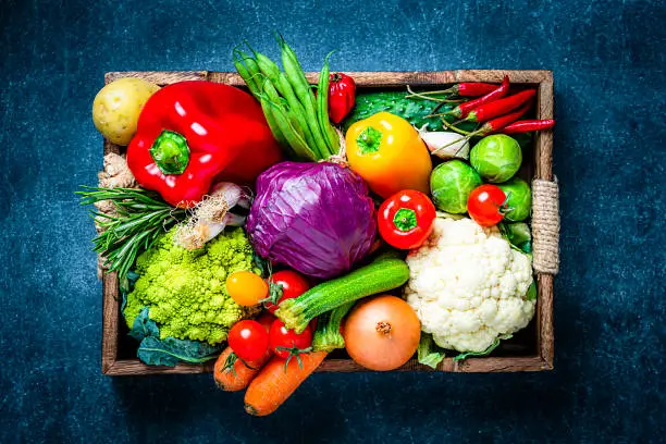 Healthy food: top view fresh multicolored organic vegetables for preparing a healthy meal arranged in a crate shot on dark blue table. Vegetables included in the composition are tomatoes, onion, carrot, green beans, bell pepper, chili pepper, herbs, cabbage, potatoes, among others. High resolution 42Mp studio digital capture taken with Sony A7rII and Sony FE 90mm f2.8 macro G OSS lens