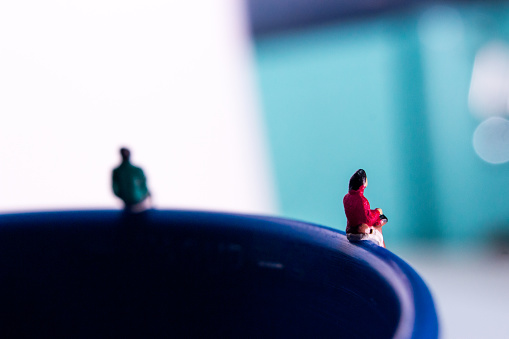 Una mujer en miniatura con abrigo rojo sentado en el borde de la taza de plástico azul photo