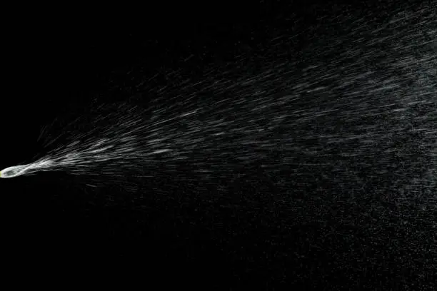 Photo of Liquid water spray mist from perfume bottle isolated on black. Aerosol splash background.