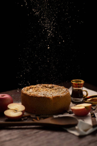 istock Sprinkling sugar powder from above on homemade apple pie with ingredients on rustic dark background. Classic autumn Thanksgiving dessert - organic apple pie. 1249232069