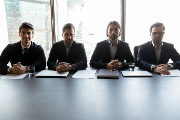 cuatro hombres de negocios serios y seguros sentados en la mesa en la sala de juntas - exam business caucasian board room fotografías e imágenes de stock