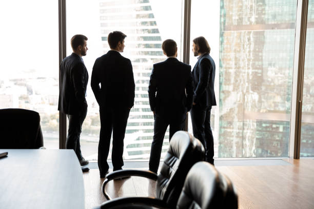 istock Rear view four confident businessmen looking through panoramic window 1249232586