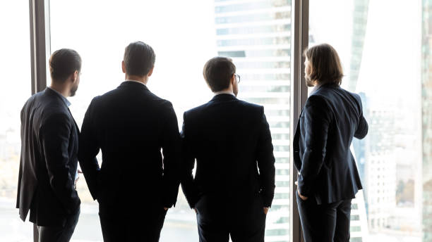 istock Rear view four confident successful businessmen looking through window 1249232587